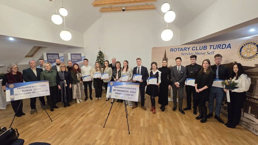 Elevii premiați și membrii clubului, în fața bannerului Rotary Club Turda, cu panourile „Excelență în educație — șef promoție 2024, premiu 1.500 lei” și „bursă 2024, în valoare de 6.000 lei”